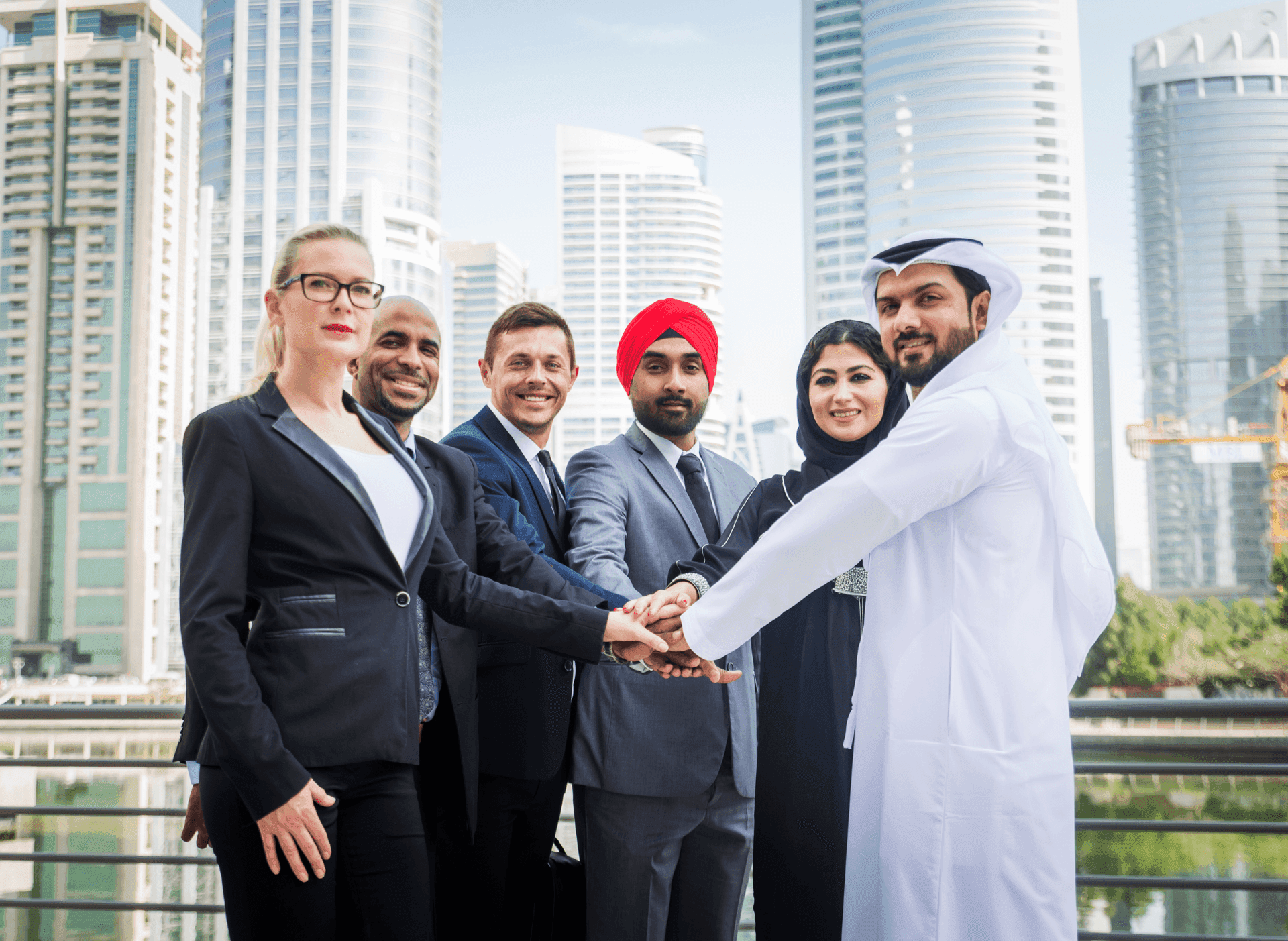 Diverse business team joining hands outdoors with skyscrapers in the background.